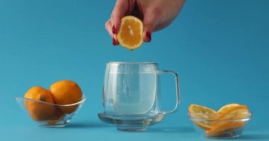Kadın eli stüdyoda mavi arka planda suya damlayan taze limon sıkar. Turunçgil meyveli sağlıklı içecek. Limonatanın yavaş çekim reklamı ve üretimi