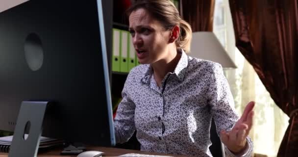 女性労働者は怒りを取得し 半ライトオフィスのテーブルに座ってコンピュータを介してオンラインで話すことを誓う 仕事の遅い動きによる積極的な行動 — ストック動画