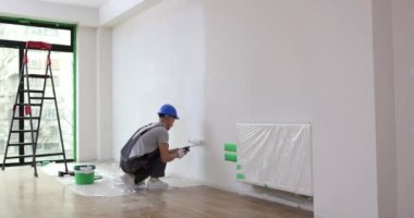Eldivenli adam boya silindirli duvar tutuyor. Sanatçı evin duvarını silindir ve beyaz boyayla boyuyor.