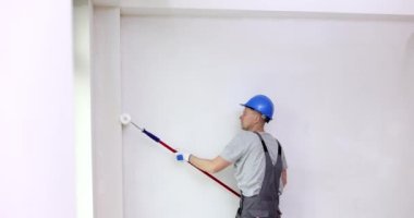Miğferli bir ressam duvarları silindirle boyar. Boyama, onarım ve ev geliştirme.