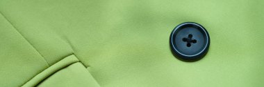 Black button is sewn on green cotton fabric closeup. Buttons for clothes features and selection