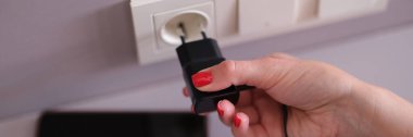 Woman with mobile phone charger in a socket on wall. Charging mobile smartphone concept