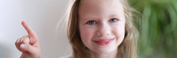 Портрет веселой улыбающейся девочки указывает пальцем в сторону. указание направления рекламный баннер