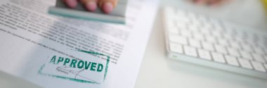 Closeup of a person hand stamping green approved seal on text approved document on table. Contract form and business agreement with partner