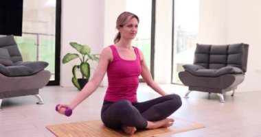 Genç kadın dambılları kafasının üzerine kaldırarak egzersiz yapıyor. Oturma odasında dambılı güzel trenler.