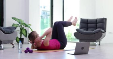 Kadın evdeki halıda basın mensuplarını çekti ve dizüstü bilgisayardan video rehberini izledi. Uzak ev fitness eğitimi