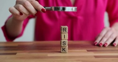 Kadın, tahta risk bloklarını büyüteçle inceliyor. Karar verirken risk yönetimi