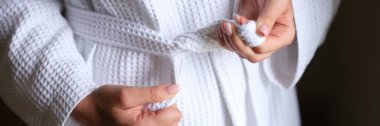 Female hands tying white bath robe closeup. Comfortable clothes for home concept