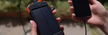 Hands holding mobile phone with external battery connected to it with solar battery closeup. Saving electricity concept