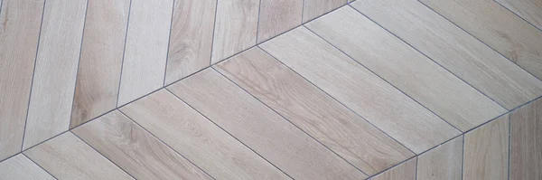 Floor lined with herringbone wooden laminate or parquet background closeup. Finishing of apartments concept