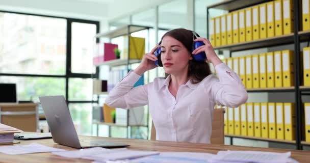 女人戴上耳机 在办公室的笔记本电脑上工作 有声办公室概念的主动式降噪耳机 — 图库视频影像