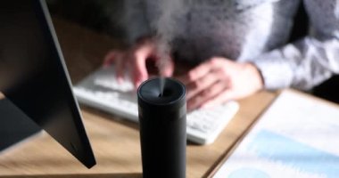 Serbest çalışan bir kadın, ofisteki işyerinde dizüstü bilgisayarla nemlendirici kullanıyor. İş yerinde ya da evde iklim kontrolü