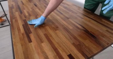 Ahşap yüzeyi kaplayan koruyucu eldivenli marangoz elleri yakın plan. Marangozluk mobilyaları cilalıyor.