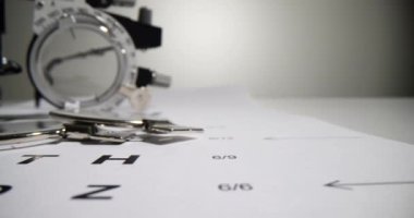 Arka plandaki çerçevede mercek seçimi için gözlük, göz doktorunun masasıdır. Miyopluk, miyop ve astigmatizm tedavisi