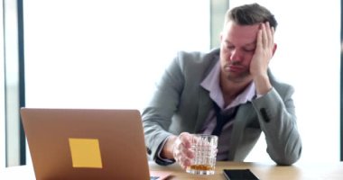 Drunk sad businessman holding glass with alcohol at workplace. Emotion stress depression and alcoholism at work
