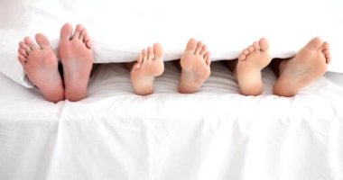 Legs of woman with two men in bed in bedroom. Polygamy in men and women