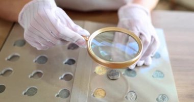 Numismatics and old collectible silver coins. Collector with magnifying glass in gloves holds ancient coin