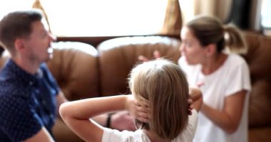 Rear view of child girl covers ears with hands while parents are quarreling. Child suffering from parental quarrels neglect or divorce
