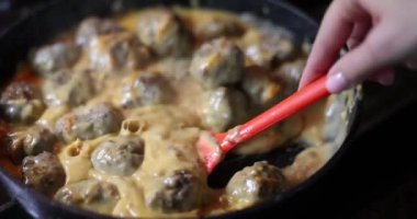 Cook stirs meatballs in creamy sauce in pan. Meatballs at home