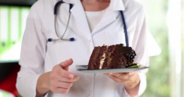 Nutritionist doctor holds piece of cake and warns about dangers of sweets. Sugar benefits and harms to human health