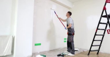 Boyacı dairenin duvarını beyaz fırçayla boyuyor. Boyama ve ev tamiri.