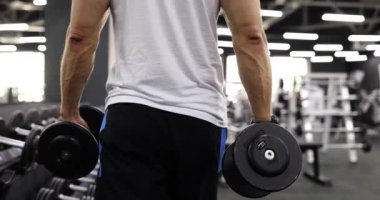 Spor salonunun arka gözünde dambılı olan erkek sporcu. Spor salonunda spor eğitimi.