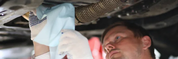 Auto mechanic inspects car leak and suspension parts of raised car with napkin at repair station. Service and repair auto concept