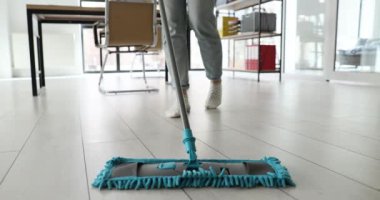 Ofiste bir kadın yerleri paspasla yıkıyor, bacakları yakın plan. Çalışma alanının dezenfeksiyonu, temizlik