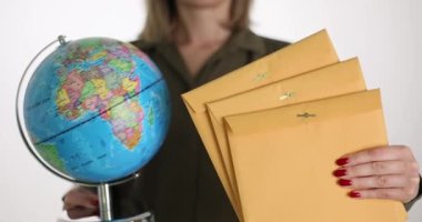 İş kadını elinde sarı zarflar ve yakın plan bir küre tutuyor. Uluslararası kurye hizmeti kavramı