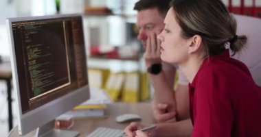 Bir kadın ve bir erkek bilgisayar ekranındaki koda bakıyorlar, yakın plan. Bir yazılım uygulaması test ediliyor