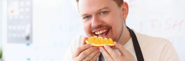 赤い笑顔の男性料理人はオレンジを噛んでいる 果物と健康食品の概念 — ストック写真