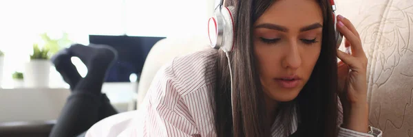 戴耳机的年轻女性正在沙发上放松 并在网上用智能手机听音乐 音乐和教育应用于电话 — 图库照片
