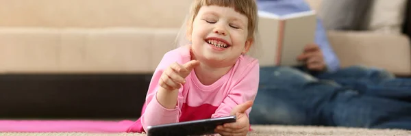 Μικρό Χαμογελαστό Κοριτσάκι Smartphone Βρίσκεται Στο Πάτωμα Στο Παρασκήνιο Μπαμπάς — Φωτογραφία Αρχείου