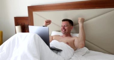 Yetişkin adam yatakta yatarken laptopta başarıyı kutluyor. Çevrimiçi ağda iyi haberlerin ve başarıların başarısı