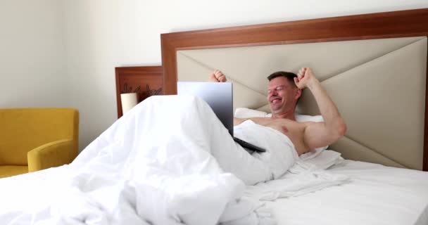 Ευτυχισμένος Όμορφος Άντρας Ξαπλώνει Στο Κρεβάτι Και Γελάει Και Διαβάζει — Αρχείο Βίντεο