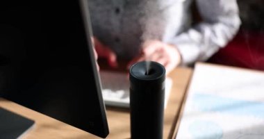 Ofis masasında hava nemlendirici cihazı var. Kadın yönetici çalışma masasında otururken gerekli yağ dağıtıcısını kullanıyor