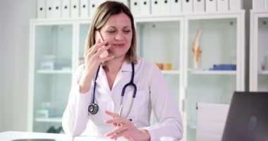 Mutlu genç doktor masada oturur ve hastayla telefonda konuşur. Pozitif kadın hemşire hastayla uzaktan konuşuyor.