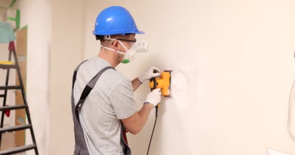 保護マスクやゴーグルのホーム改善労働者は 壁のレベルの表面にグラインダーで動作します 石膏で壁をレベリング — ストック動画