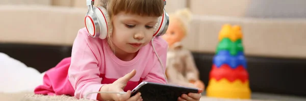 Mała Dziewczynka Słuchawkach Trzyma Smartfona Leżącego Podłodze Dzieci Oglądają Kreskówki — Zdjęcie stockowe