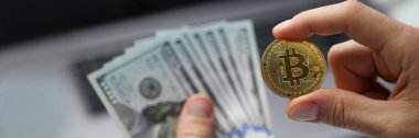 İnsan eli 100 dolarlık banknotları ve altın bitcoin paraları tutar. Kripto para birimi geliri ve mali yatırımları