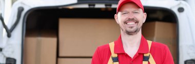 Gülümseyen erkek kurye arabanın arka planında kutusunu çekiyor. Mal ve paket teslimatı kavramı