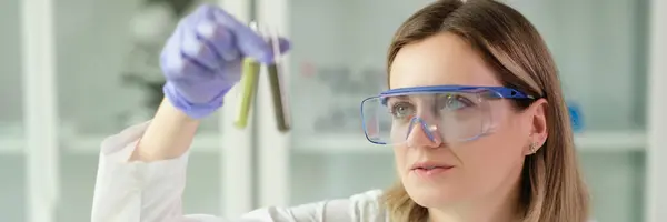 戴防护眼镜的女化学家在实验室拿着装有液体的试管 制药企业概念 — 图库照片