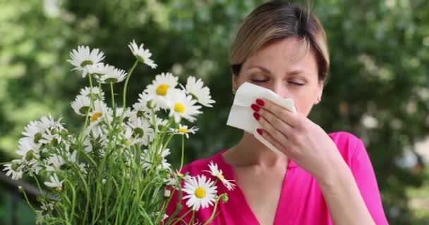 アレルギー症状を持つ若い女性は カモミールの花の花束を保持公園に立っている間 鼻を吹く 病気の女の子はくしゃみと花粉症のために組織に彼女の鼻を吹く — ストック動画
