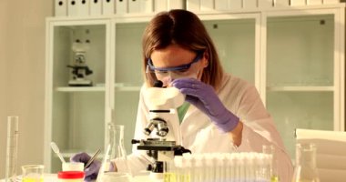 Kadın bilim adamı mikroskobu inceliyor ve bilimsel buluşlar için araştırma notları yazıyor. Bilimsel veriler için not defteri olan ya da laboratuarda sonuç alan kadın ya da tıp uzmanı