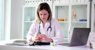 Akıllı telefon uygulaması kullanarak klinikteki güzel terapist danışmanları. Gülümseyen kadın doktor cep telefonu teknolojisi cihazı tutuyor mesaj gönderiyor ve uzaktan kumandalı hastaya danışmanlık yapıyor.