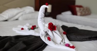 Otel odasında bir hediye ve gül yapraklı çift yataklı kuğulu beyaz havlular. İki kişilik romantik kompozisyon