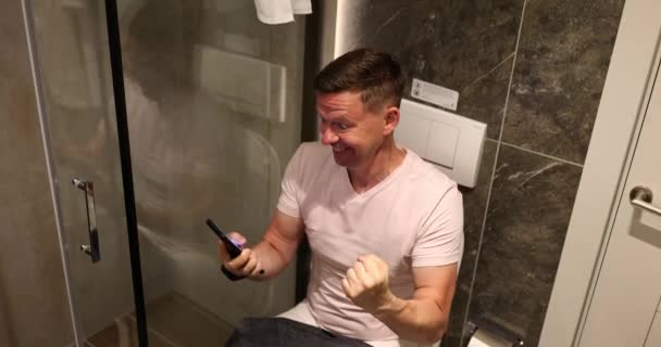 男人笑着在厕所里看电话 快乐快乐意外的消息 — 图库视频影像