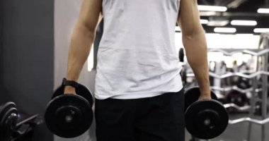 Spor salonunda dambıllarla yürüyen bir sporcu. Beden eğitiminde kuvvet.