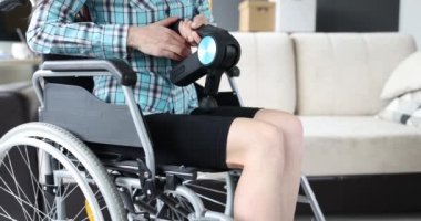 Tekerlekli sandalyedeki bir kadın, bacağına perküsyon masajlı 4K filmle masaj yapıyor. Engelli konsepti için ev rehabilitasyonu