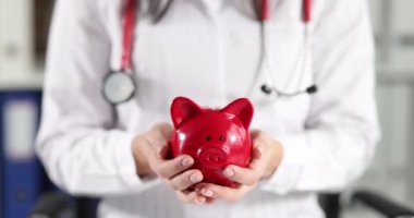 Doctor holding red piggy bank in clinic closeup 4k movie slow motion. Investment in medical education concept
